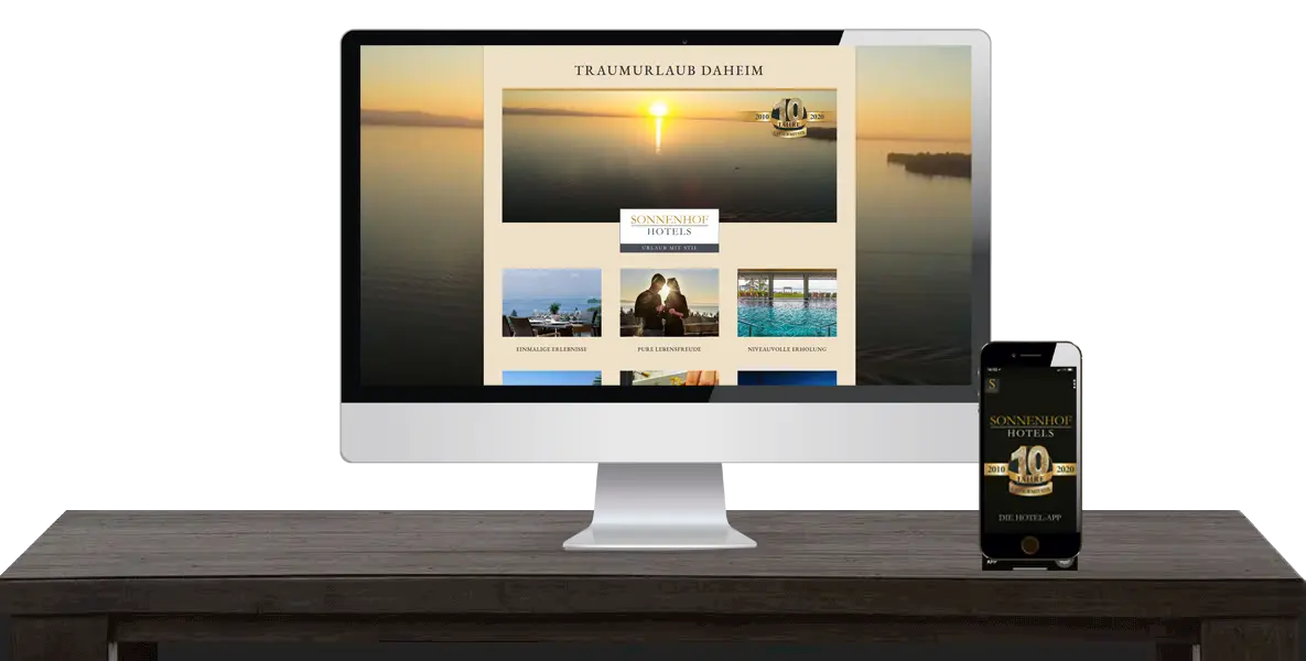 Ein Computer und ein Smartphone zeigen eine Hotelwebsite an, beide stehen auf einem dunklen Holzschreibtisch.